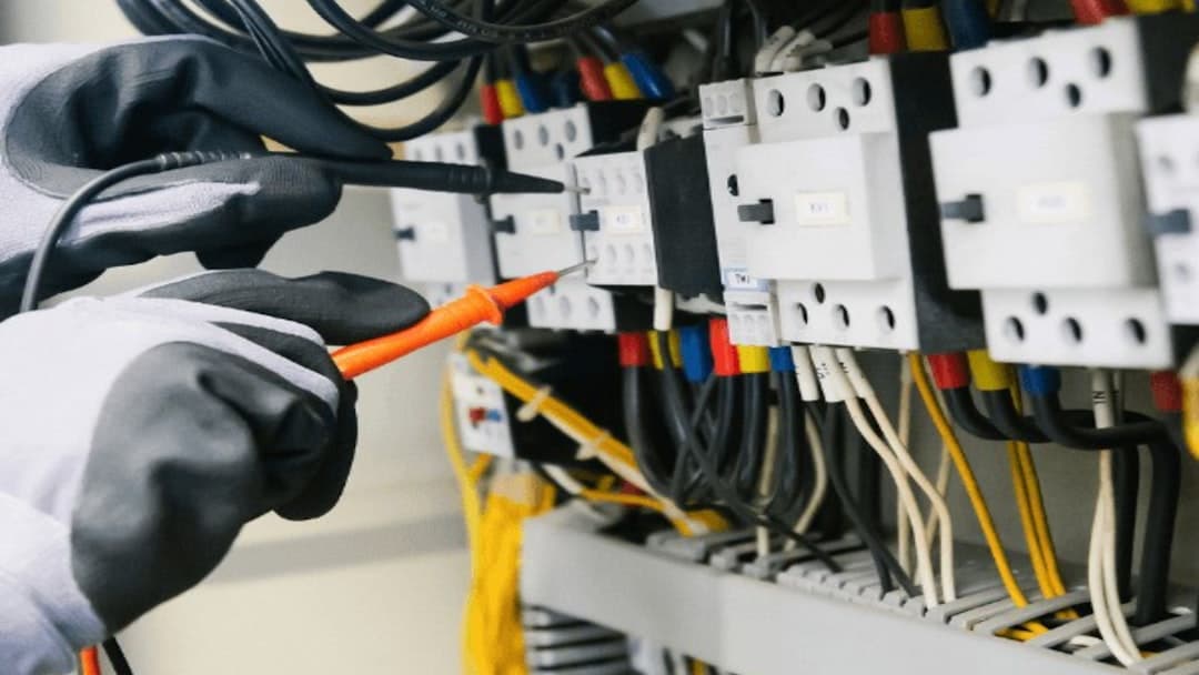 Experienced engineer probing terminals inside an electrical control panel with a multimeter